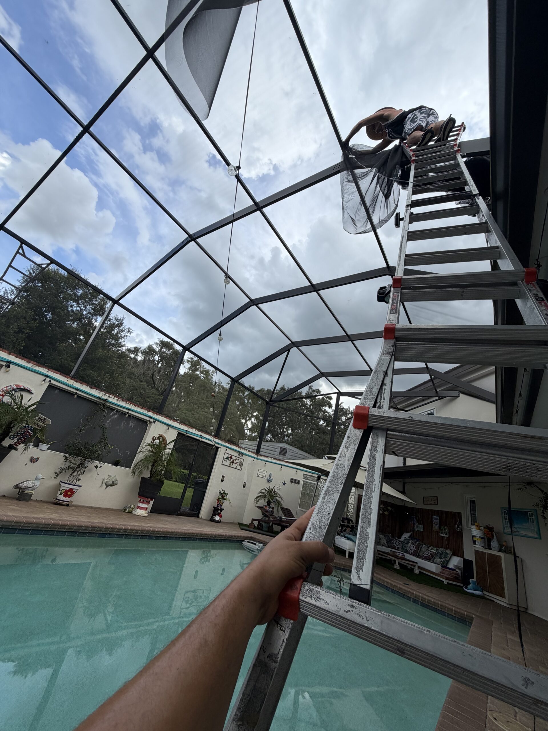 Two-story pool cage rescreening work in New Tampa Florida with roof screening being installed